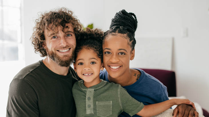 Bild einer Familie aus Vater, Mutter und kleinem Jungen, die glücklich lächeln und sich in den Arm nehmen