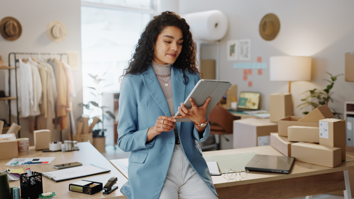 Bild einer Frau mit lockigem, brauem Haar, die in ihrer Wohnung ein iPad in ihren Händen hält