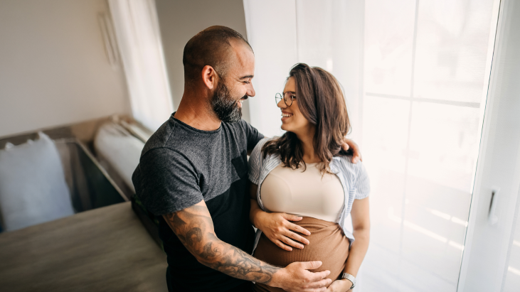 Bild eines glücklichen Paares, bei dem der Mann seine Hand auf den schwangeren Bauch der Frau legt
